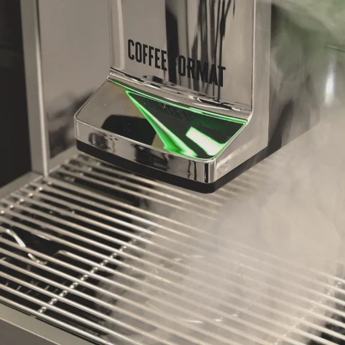 Coffee Format DUKE — zbliżenie wylewki i stalowej kratki podczas pracy ekspresu